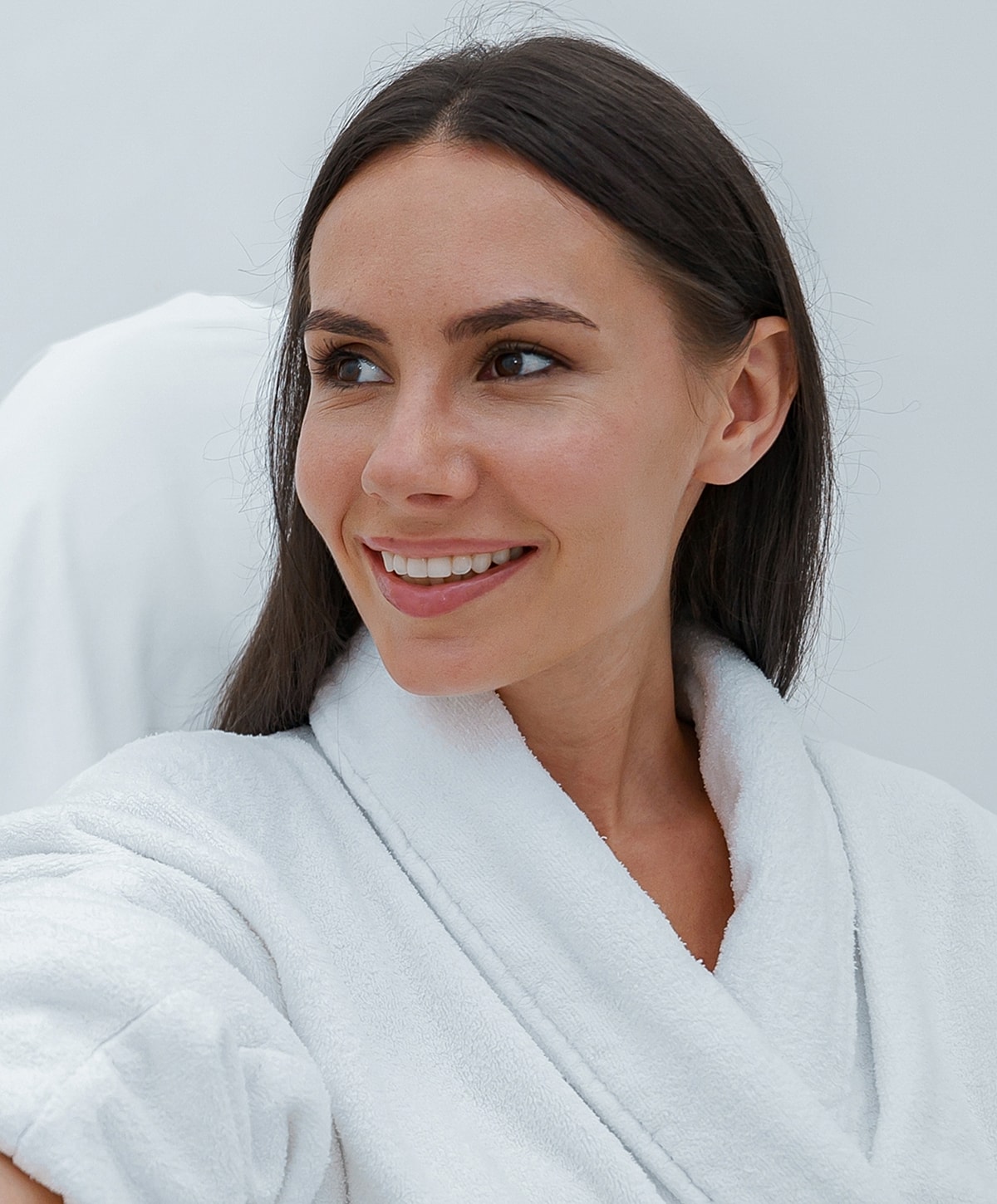 Smiling woman in white bathrobe against plain backdrop